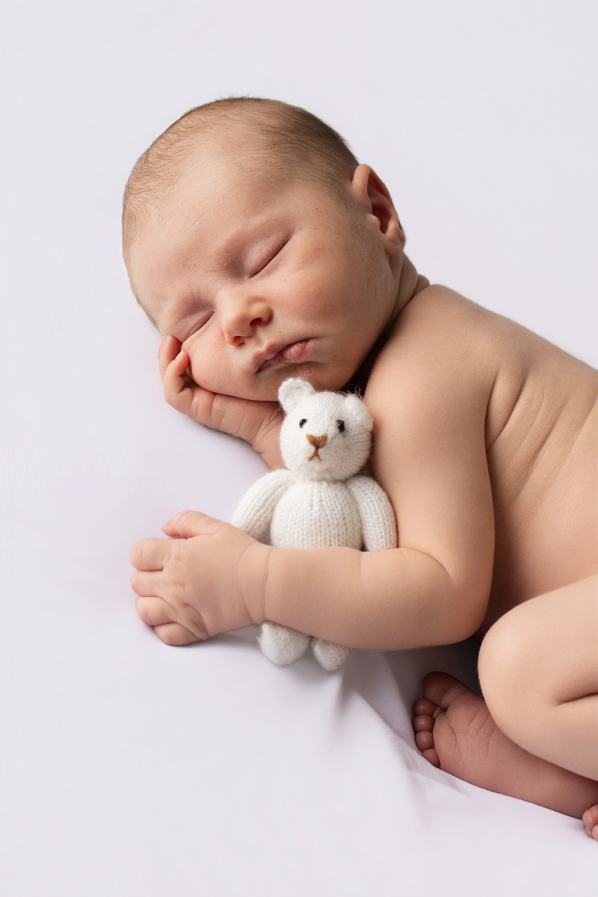 Newborn curled up with a soft teddy bear on cream