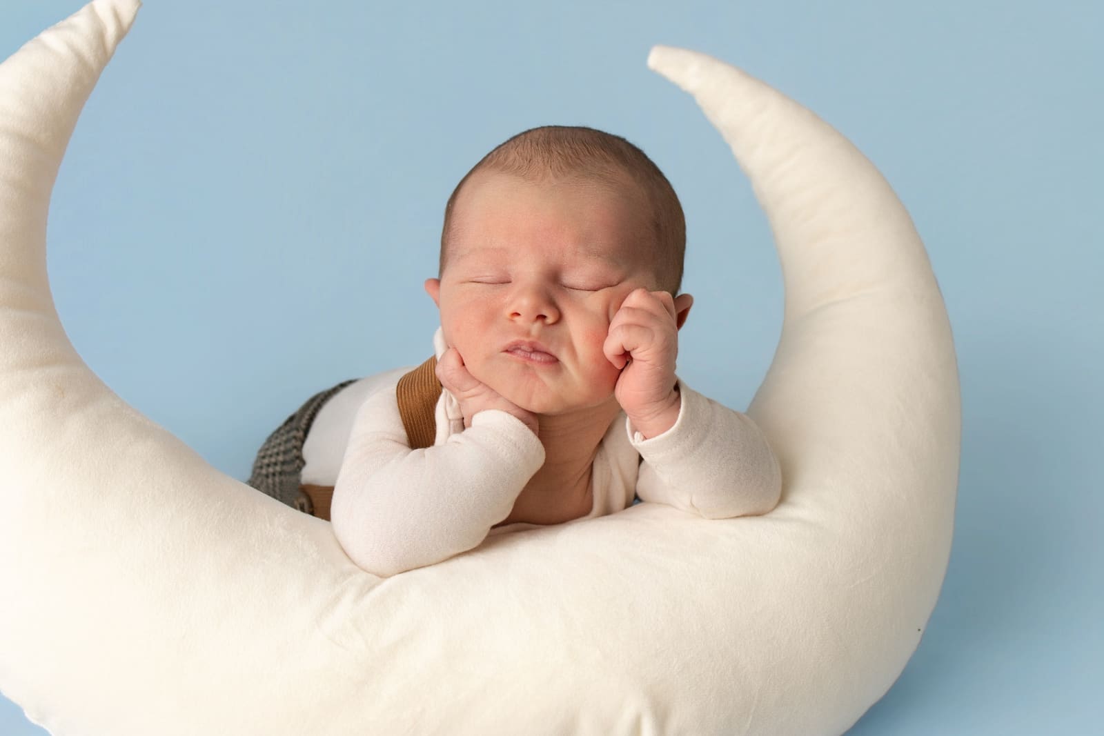 Sleeping newborn curled in a moon prop on a soft cream backdrop