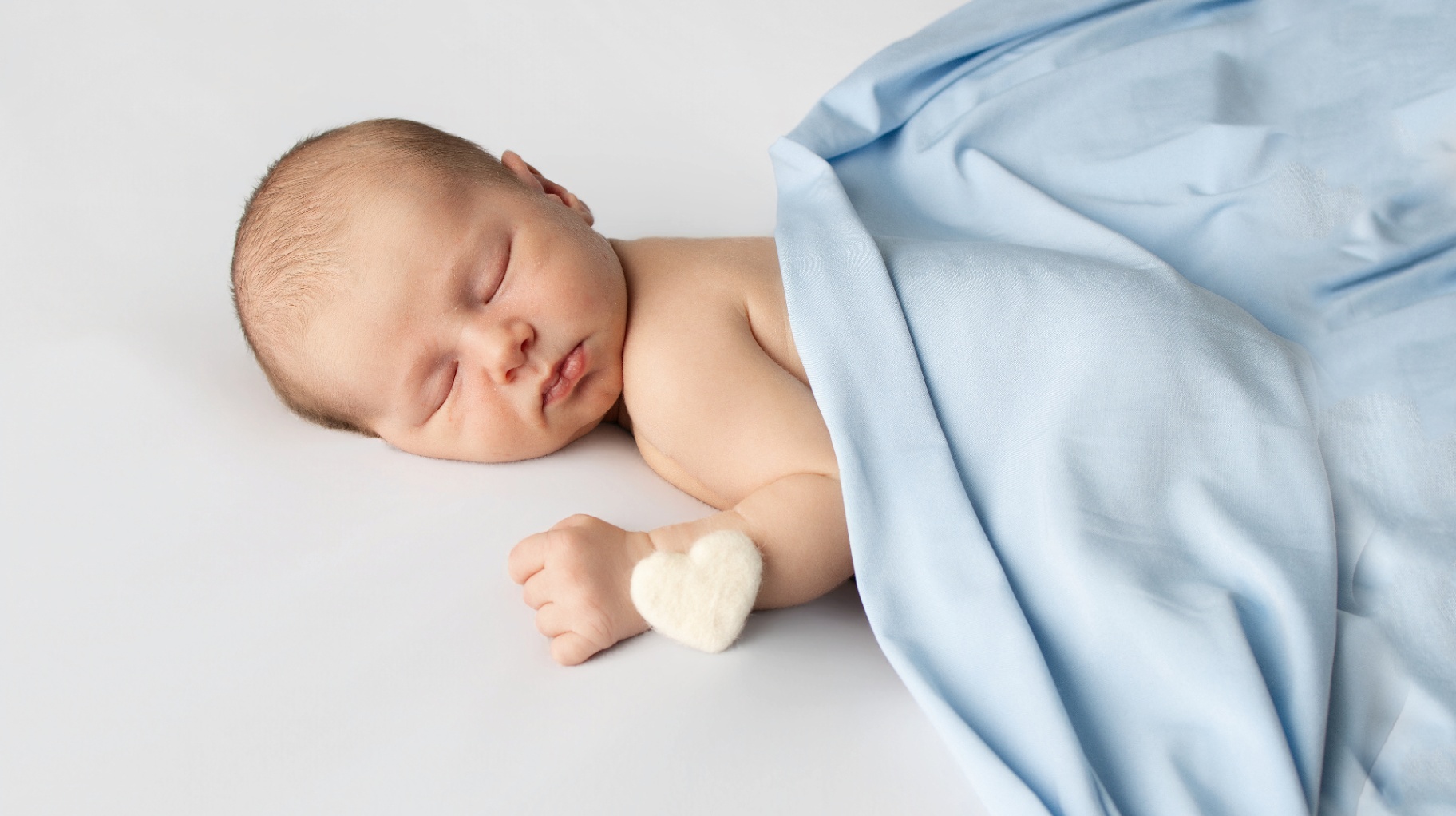 Sleeping newborn wrapped in soft blue with a tiny heart detail